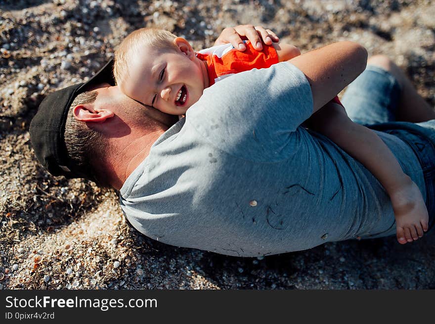 Funny portrait of a father and son, while they are playing on the beach, lying on the sand, embracing and smiling