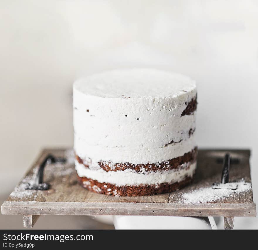 chocolate cake smeared with white cream. stands on a wooden stand