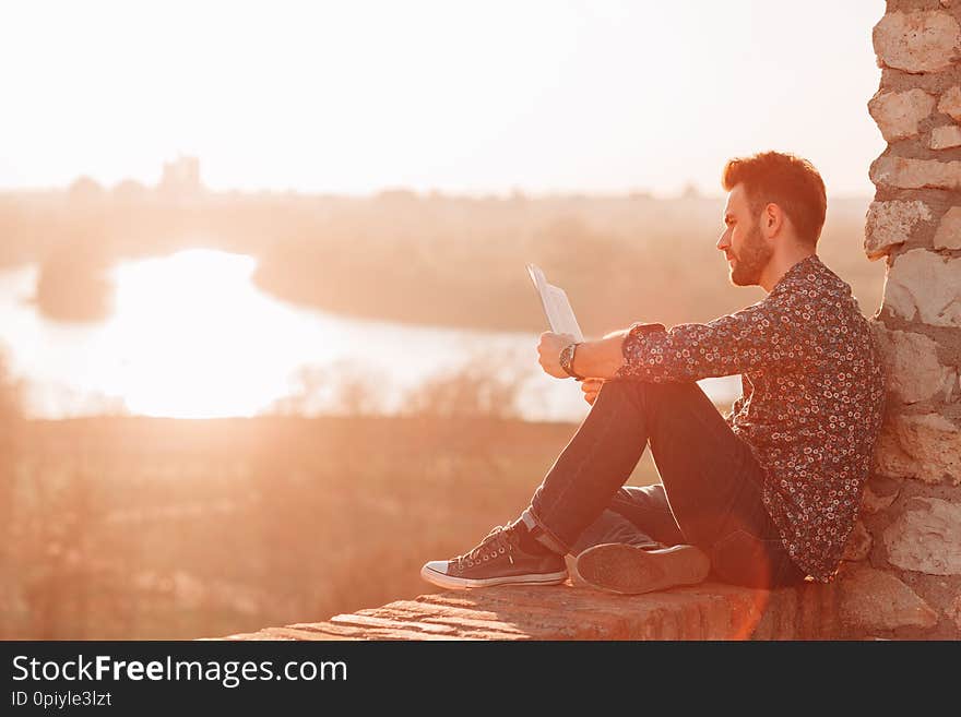 Young man reading a book outdoors in sunset