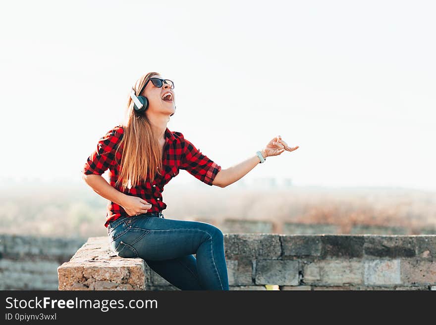 Young woman listening to the music on headphones playing imaginary guitar outdoors