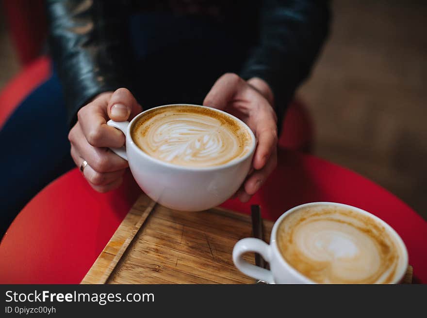 Hand holding a white cups of hot latte coffee of cappuccino coffee on red table in cafe