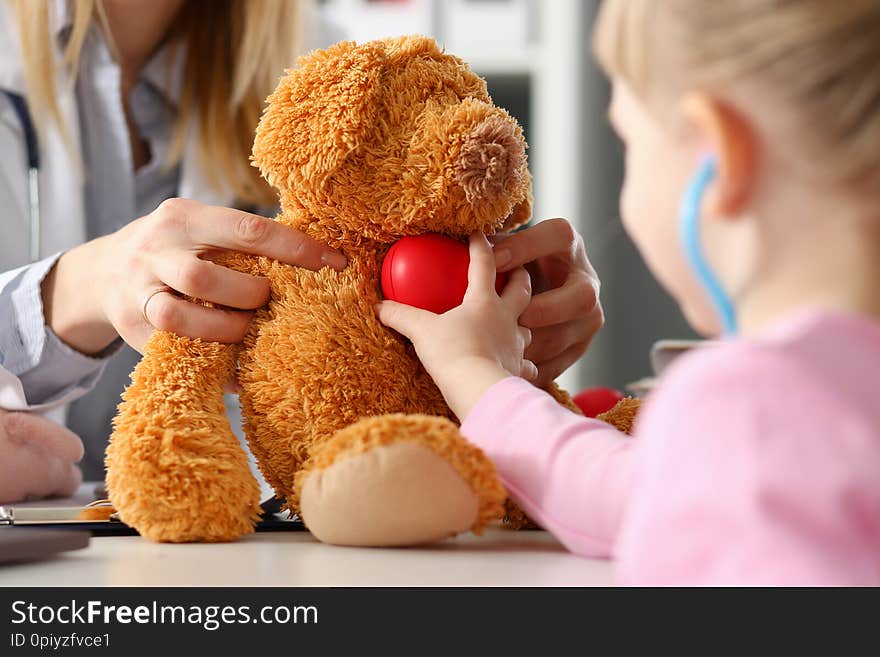 Little girl hold in arms toy red hear playing with teddy bear while visiting doctor