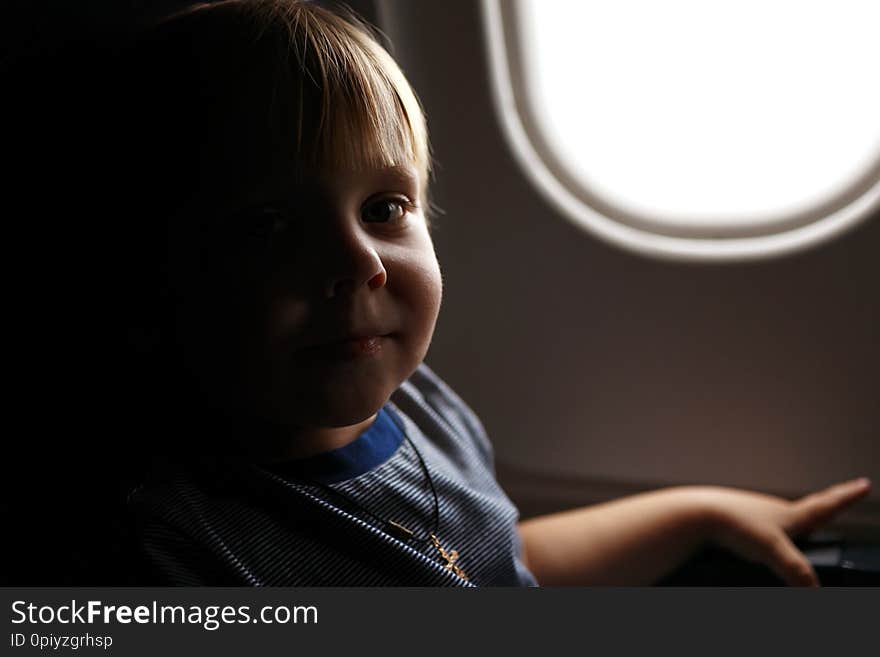 Smiling small blonde hair toddler boy sitting in jet airplane next to the plane window and looking at his parents. Smiling small blonde hair toddler boy sitting in jet airplane next to the plane window and looking at his parents