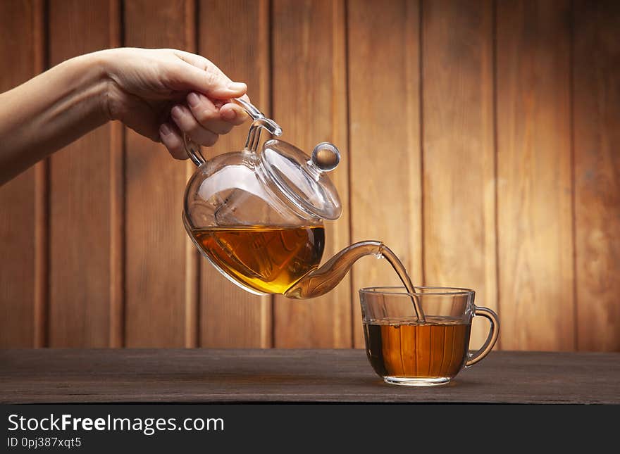 Woman hand poured cup of tea on a wooden table from a teapot.