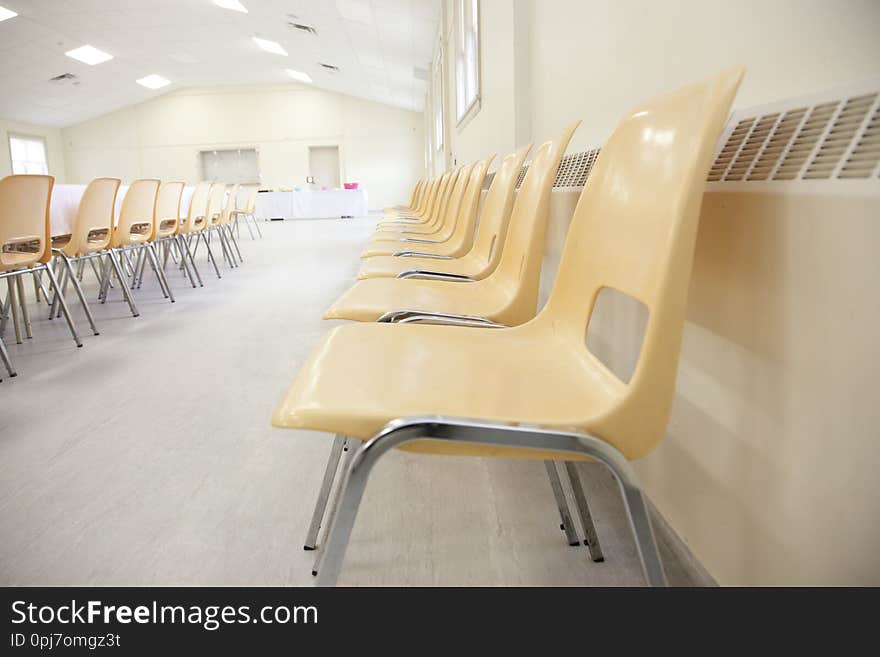 long line of plastic chairs against a heater in a hall. long line of plastic chairs against a heater in a hall