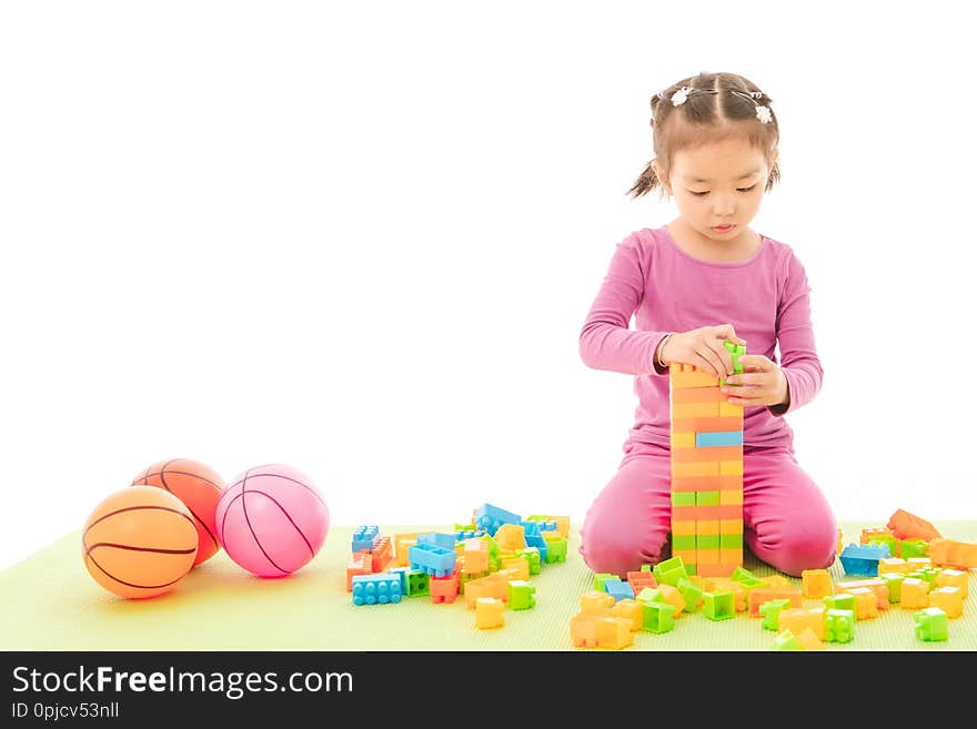 Portrait of cute little Asian girl in purple t-shirt and pants happily standing on green yoga mat holding multi-colorblocks toy and plastic baby toy balls on isolated white background. Portrait of cute little Asian girl in purple t-shirt and pants happily standing on green yoga mat holding multi-colorblocks toy and plastic baby toy balls on isolated white background