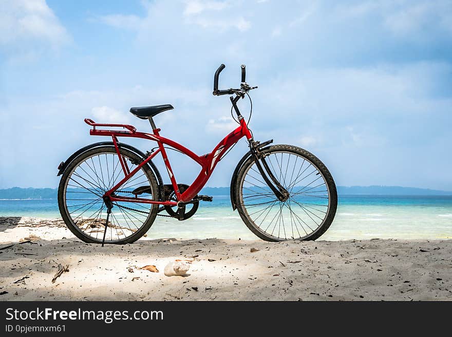 Red vintage bicycle on white sand beach over blue sea and clear blue sky background, spring or summer holiday vacation concept. Bicycle parked by the sea