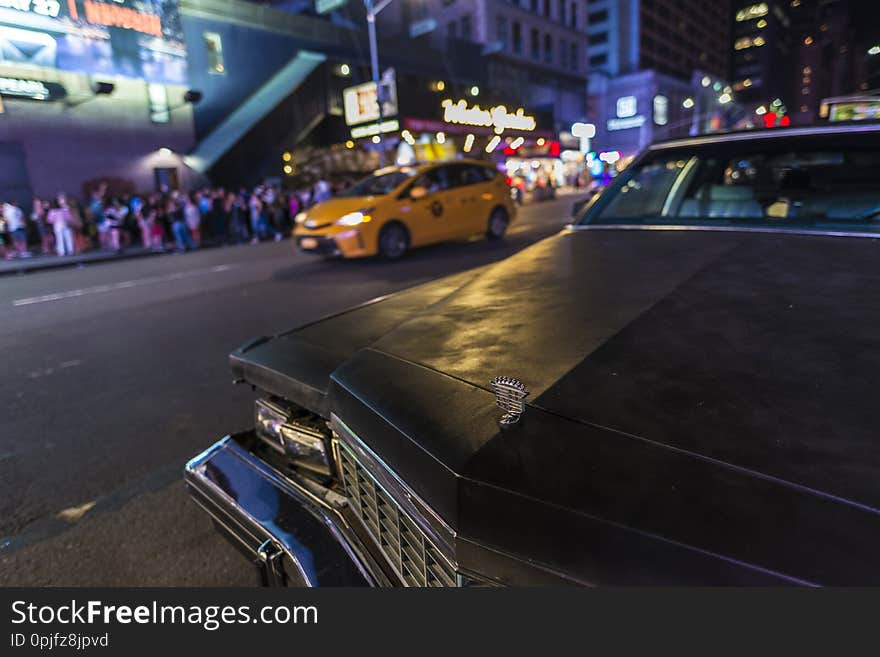 Old classic black american car parked at night on Seventh Avenue 7th Avenue next a taxi with people around in Manhattan in New York City, USA. Old classic black american car parked at night on Seventh Avenue 7th Avenue next a taxi with people around in Manhattan in New York City, USA