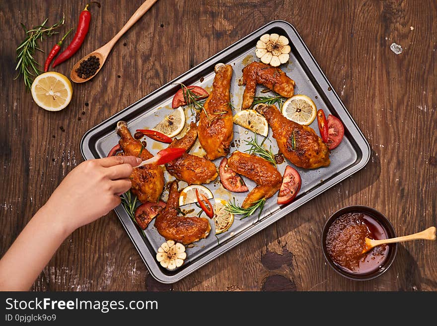 Grilled chicken drumstick and wings on baking tray over wooden table.