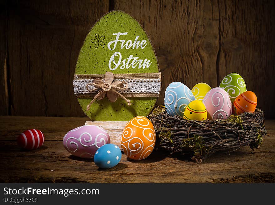 German greetings Frohe Ostern  english translation happy easter  Colorful painted eggs in birds nest basket on rustic wooden old