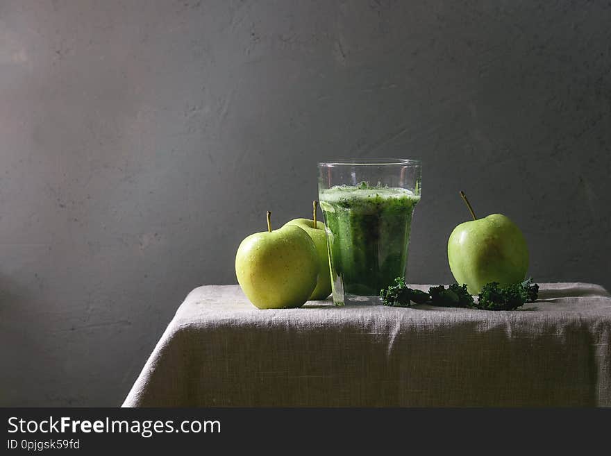 Green spinach kale apple smoothie in glass on linen table cloth with ingredients above. Healthy organic eating. Green spinach kale apple smoothie in glass on linen table cloth with ingredients above. Healthy organic eating.