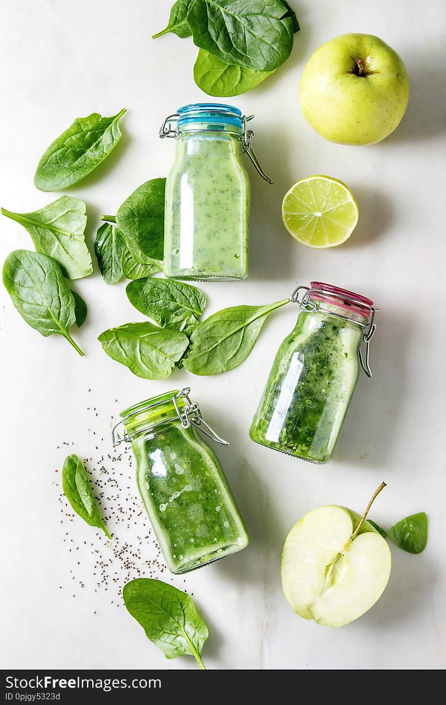 Variaty of green spinach kale apple smoothies in glass bottles with ingredients above over white marble background. Healthy organic eating. Flat lay, space. Variaty of green spinach kale apple smoothies in glass bottles with ingredients above over white marble background. Healthy organic eating. Flat lay, space