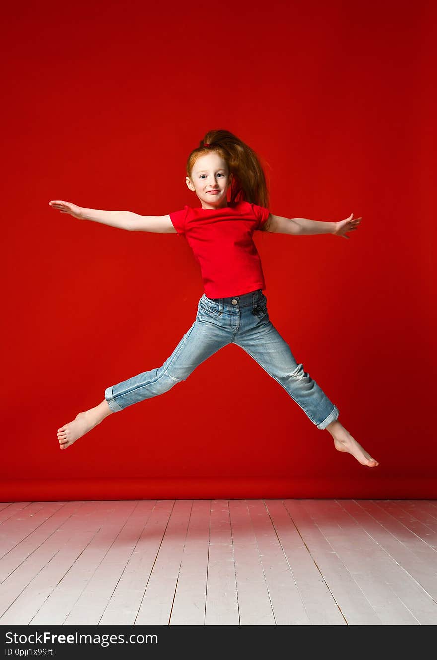 Photo of an excited jumping red-haired little girl child isolated over a red background. Watching the camera. Photo of an excited jumping red-haired little girl child isolated over a red background. Watching the camera.