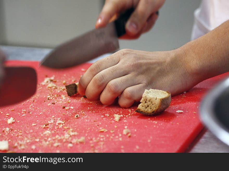 Man hands cutting bread for crutons on red cutting doard. Preparing bread for roasting croutons. Man hands cutting bread for crutons on red cutting doard. Preparing bread for roasting croutons