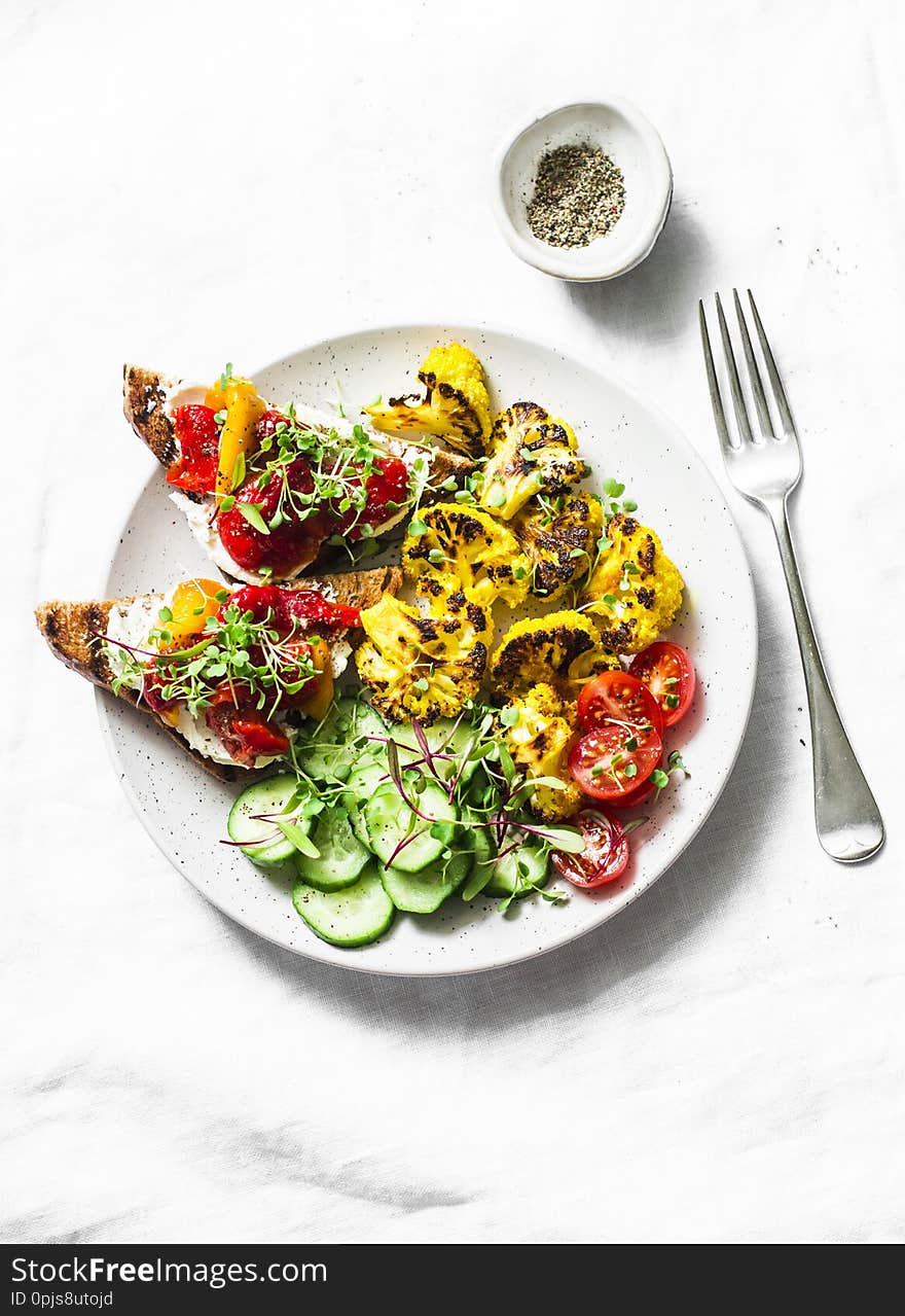 Healthy vegetarian snacks - turmeric baked cauliflower and marinated pepper, goat cheese, whole grain bread sandwiches on a light background, top view