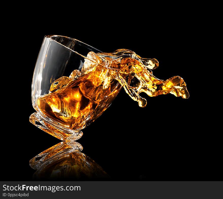 Splash of whiskey with ice cubes in glass on black background. Splash of whiskey with ice cubes in glass on black background