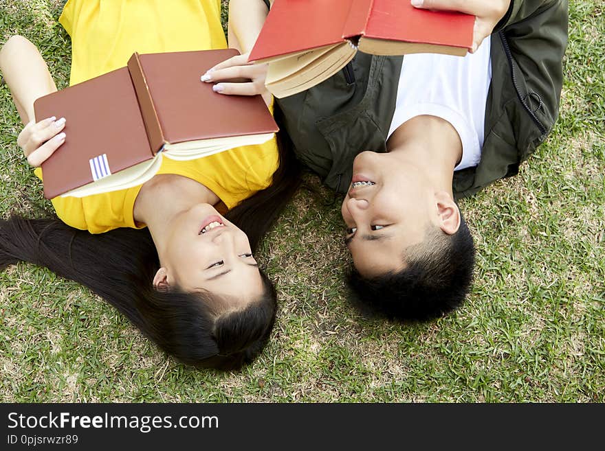 Teenagers with books lying on green grass