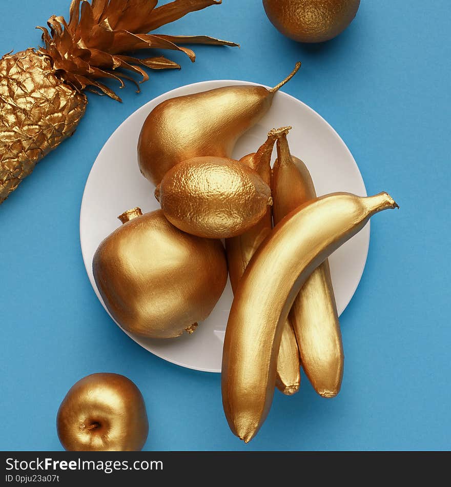 Golden fruits on plate on blue background. Shiny fruits concept