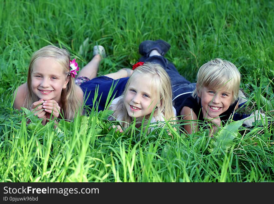 Three kids lying on green grass in park.