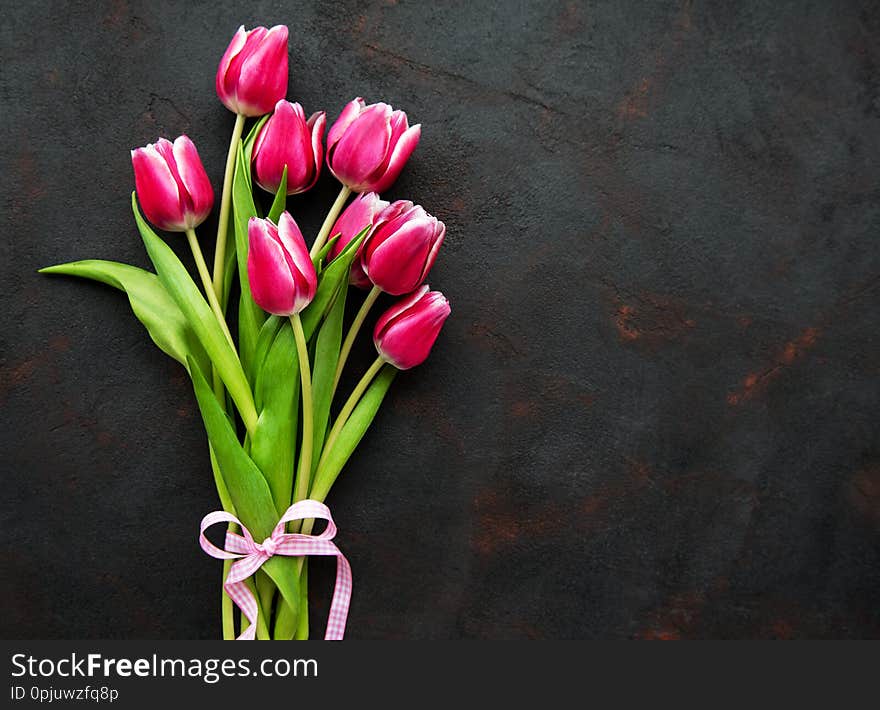 Pink spring tulips with ribbon on a black concrete background