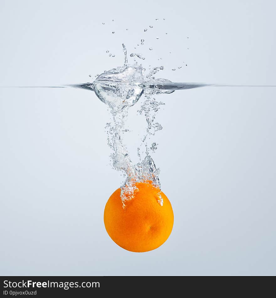 a slice of red orange falls into the water discarding a lot of splashes and drops.