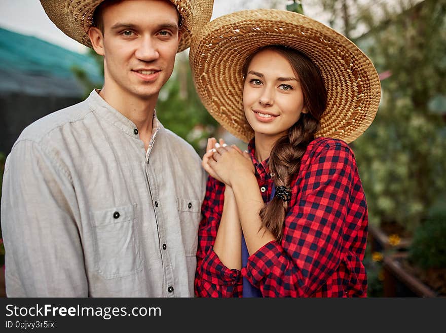 Guy And Girl Gardeners In A Straw Hats Stand Together In Garden On A Sunny Day.