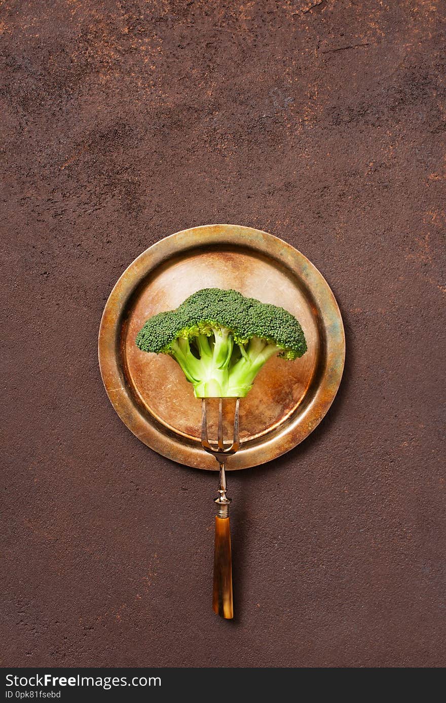 Broccoli on the vintage metal plate on the brown textured table, concept of healthy eating, top view
