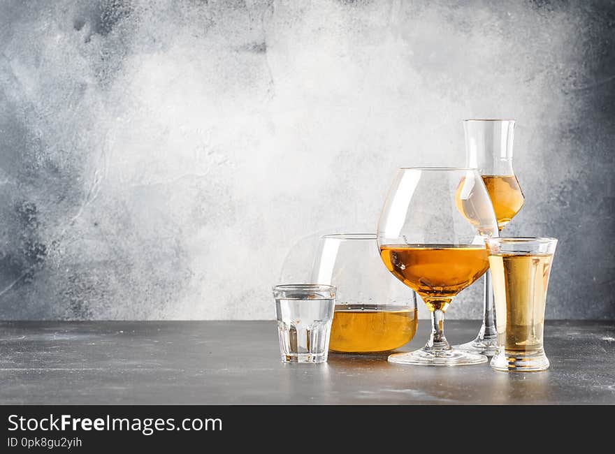 Set of hard strong alcoholic drinks and spirits in glasses in assortment: vodka, cognac, tequila, brandy and whiskey, grappa, liqueur, vermouth, tincture, rum. Gray bar counter background, selective focus, copy space