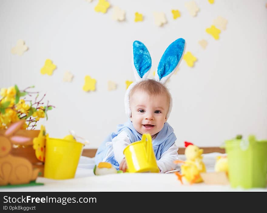 Happy baby boy with Easter bunny ears and colorful eggs and flowers