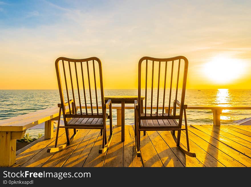 Empty wood chair and table at outdoor patio with beautiful tropical beach and sea at sunrise or sunset background for vacation and travel