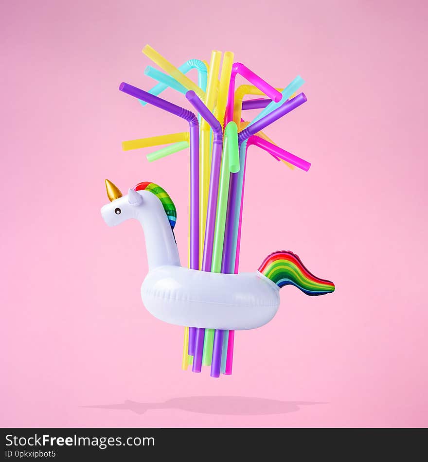 Colorful drinking straws with inflatable unicorn pool toy on pink background. Creative minimal summer concept.