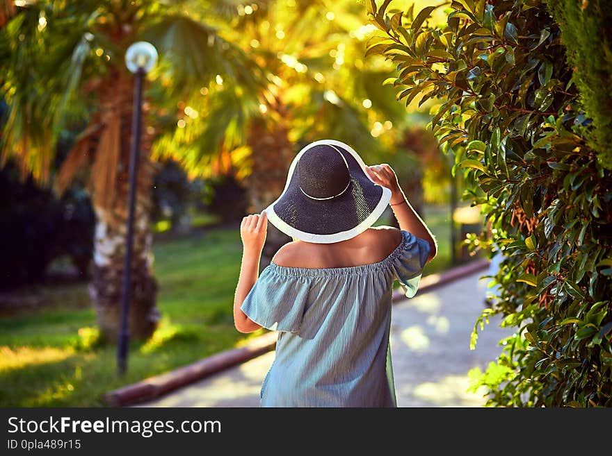 Young beautiful woman in beach hat walking under tropical palm trees at sunny day in Bodrum, Turkey. Vacation Outdoors Seascape Summer Travel Concept