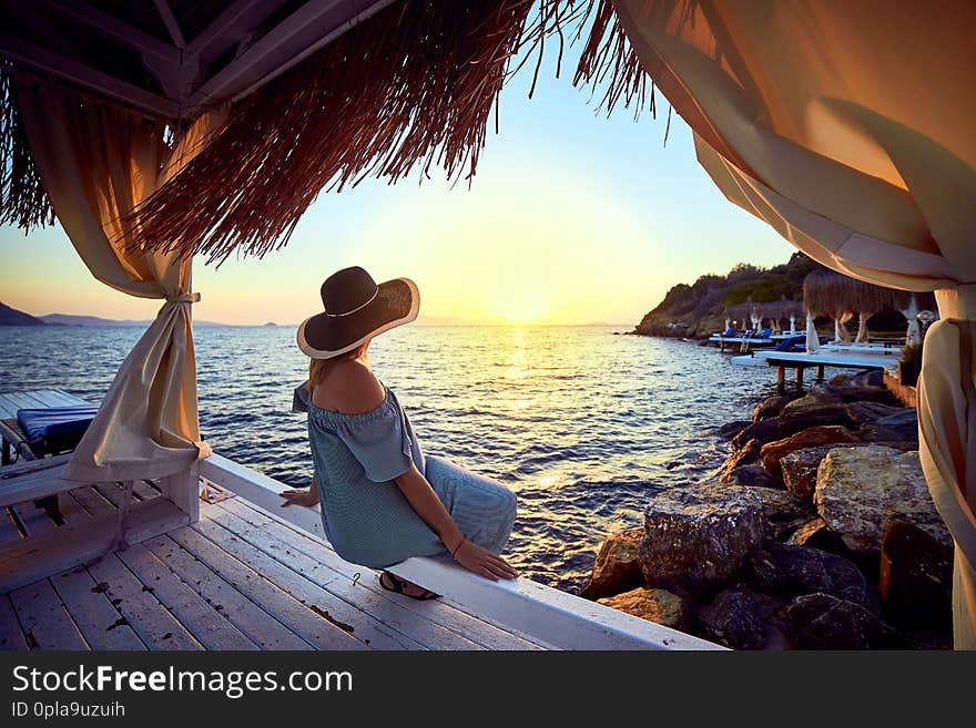 Woman in hat relaxing by the sea in a luxurious beachfront hotel resort at sunset enjoying perfect beach holiday vacation in Bodrum, Turkey. Outdoors Seascape Summer Travel Concept