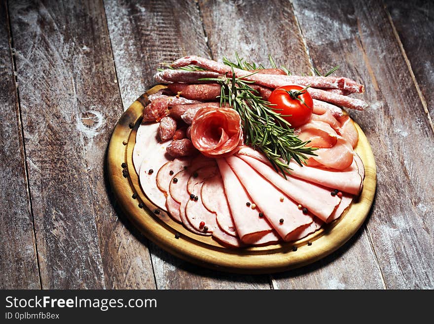 Food tray with delicious salami, pieces of sliced ham, sausage and salad. Meat platter with selection on table