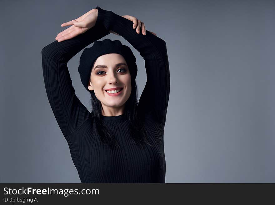 Portrait of smiling brunette girl in beret with raised handsm over gray background