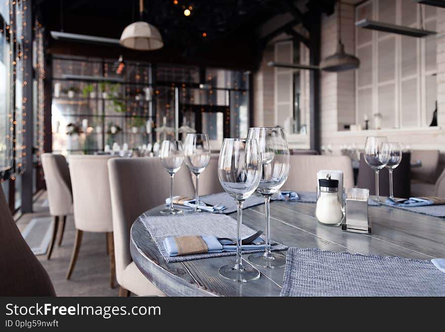 Transparent modern setting, glass vase with bouquet flowers on table in restaurant. Wine and water glasses stand on wooden table.