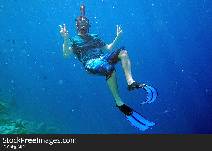 A man with diving goggles and fins snorkeling underwater.