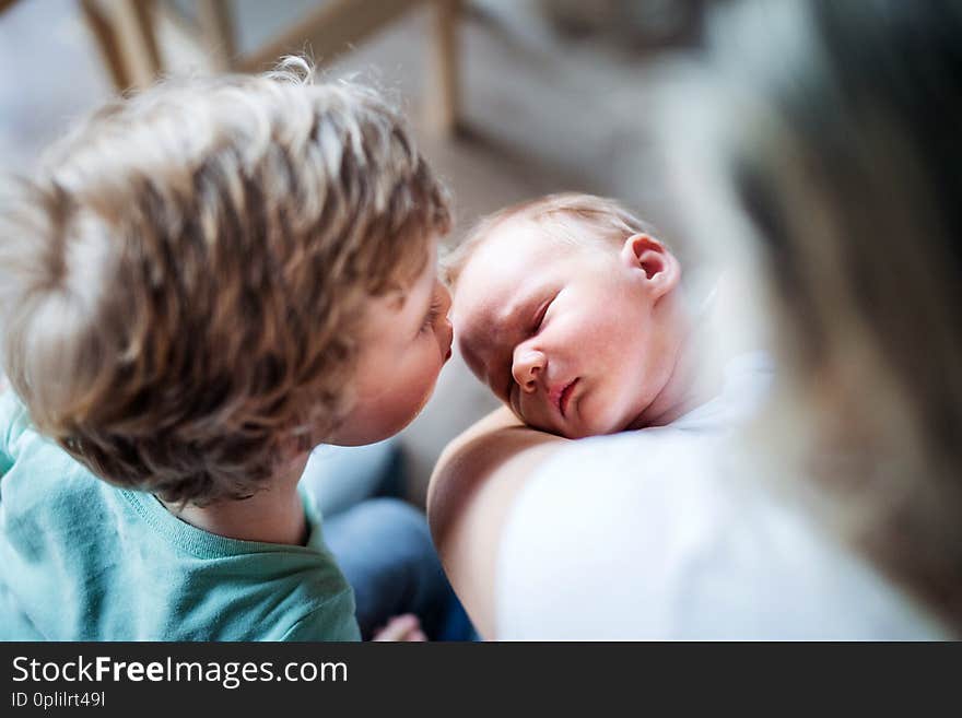 A small boy kissing a sleeping newborn baby brother at home, a mother holding him. A small boy kissing a sleeping newborn baby brother at home, a mother holding him.