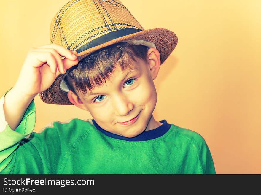 A boy in a straw hat and a green T-shirt holding a hat in a sign of greeting