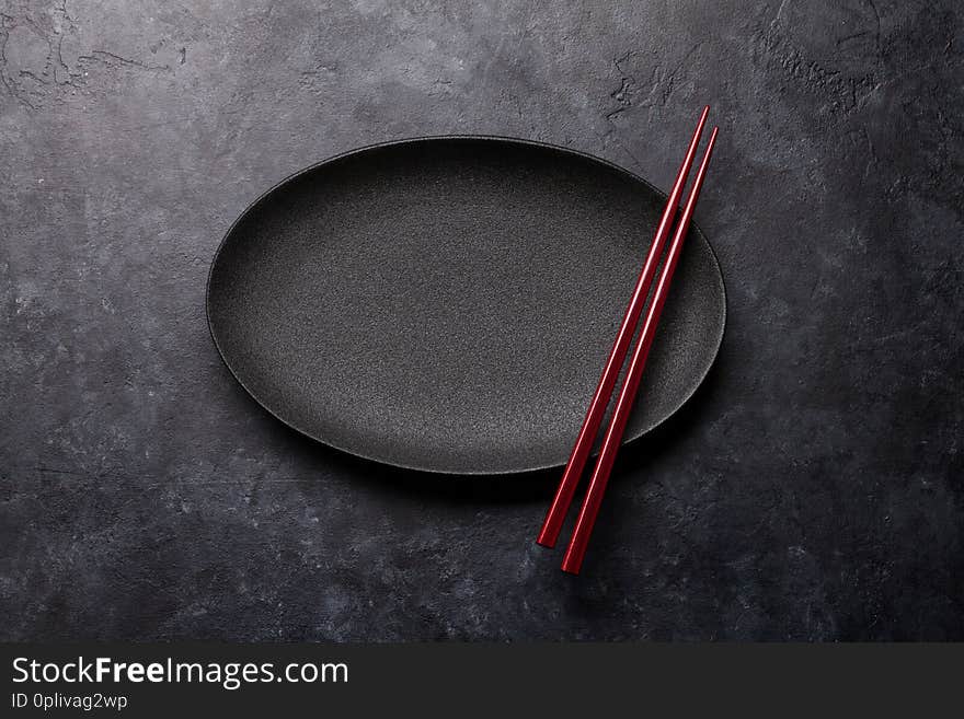 Empty plate and chopsticks over black textured table. Japanese food template. Top view with copy space. Flat lay