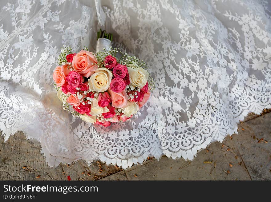 Wedding Bouquet Of Colorful Roses Lying On A White Wedding Dress.