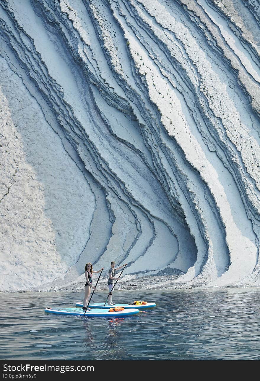 Young couple paddling on SUP board close to beautiful rock formation