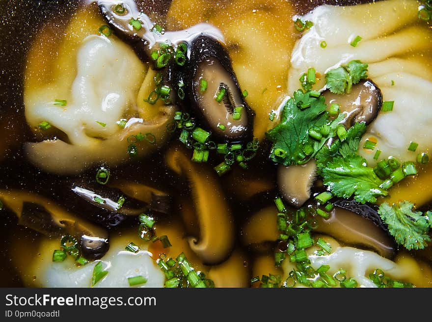 Soup wonton chicken broth with mushrooms and herbs, dark background.