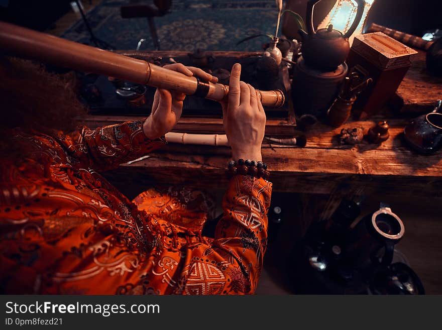 Chinese tea ceremony. Tea master in kimono performs in the dark room with a wooden interior, playing on a bamboo flute. Tradition, health, harmony. Chinese tea ceremony. Tea master in kimono performs in the dark room with a wooden interior, playing on a bamboo flute. Tradition, health, harmony.