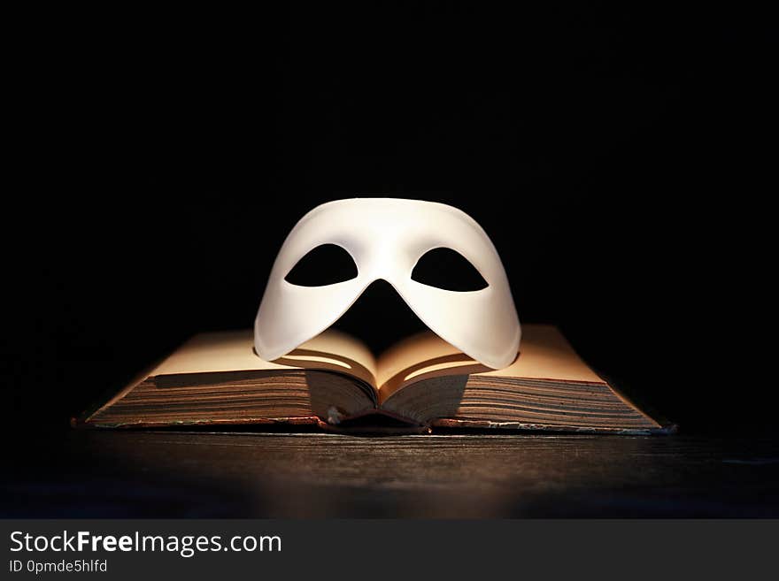 Classical white Venetian mask on old book against dark background. Classical white Venetian mask on old book against dark background