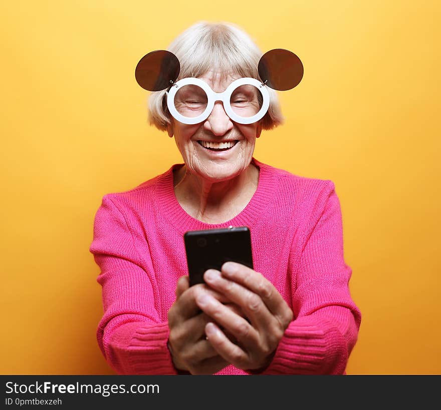 Old grandmother is talking to her grandchildren by phone, smiling and greeting them.