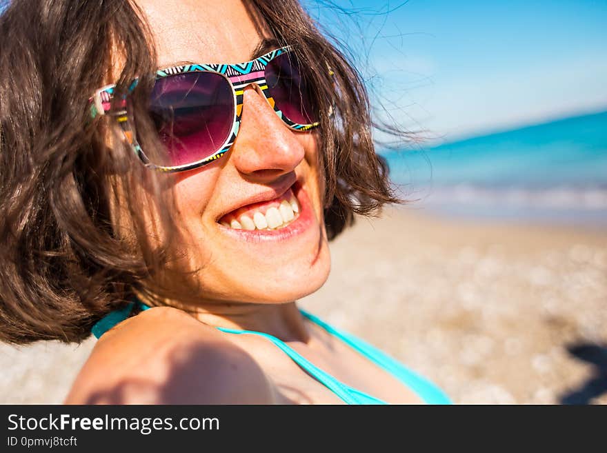 Portrait of a smiling girl in sunglasses. A woman sunbathes on the beach. Summer vacation at the seaside