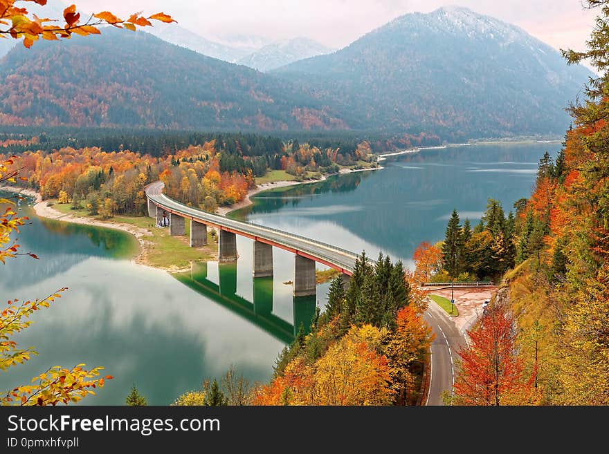 Scenic view of a curved bridge over Lake Sylvenstein with beautiful reflections on smooth water, colorful foliage by lakeside