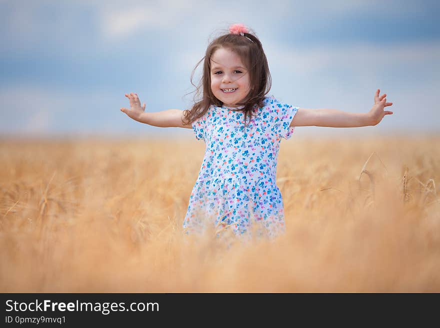 Happy girl walking in golden wheat, enjoying the life in the field. Nature beauty, blue sky and field of wheat. Family outdoor