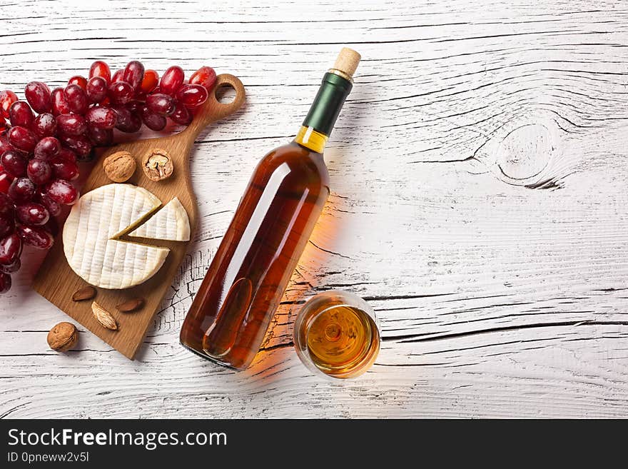 White wine bottle, grape, cheese and wineglass on white wooden board. Top view with copy space